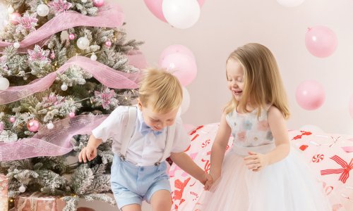 Newborn Photography Blog | Blossom Brook Studio 577 Two children holding hands and playing during a Christmas Family Photoshoot, surrounded by pink decorations and festive styling, captured as Children Christmas Photography in a bright studio.
