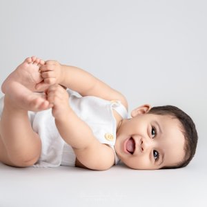 Smiling baby lying on back holding feet during a Sydney Baby Photography session at Blossom Brook Studio.