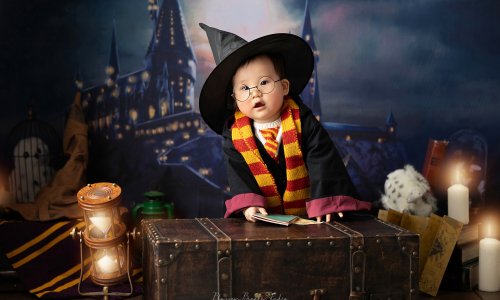 Newborn Photography Blog | Blossom Brook Studio 605 Adorable Harry Potter baby photoshoot with baby Tam wearing glasses, dressed in Gryffindor scarf, and wizard outfit holding a spellbook.